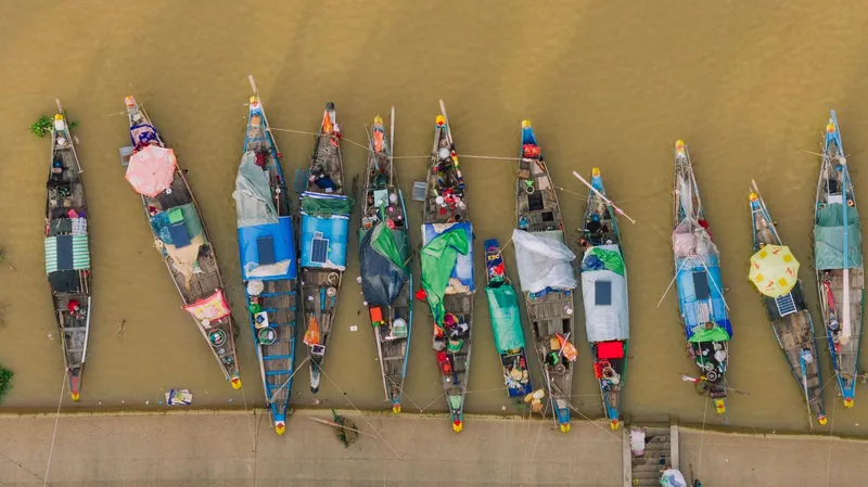 Aerial view of colorful wooden boats moored side by side along a muddy riverbank in Cambodia